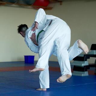 Zwei Judoka in wei&szlig;en Anz&uuml;gen f&uuml;hren einen Wurf auf einer blauen Judomatte aus.