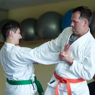 Zwei Kampfsportler in wei&szlig;en Gi mit gr&uuml;nen und orangen G&uuml;rteln im Training, wirken engagiert und interagieren.