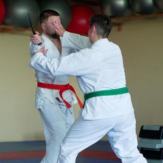 Zwei Kampfsportler im wei&szlig;en Gi &uuml;ben Techniken, einer mit rotem, der andere mit gr&uuml;nem G&uuml;rtel.