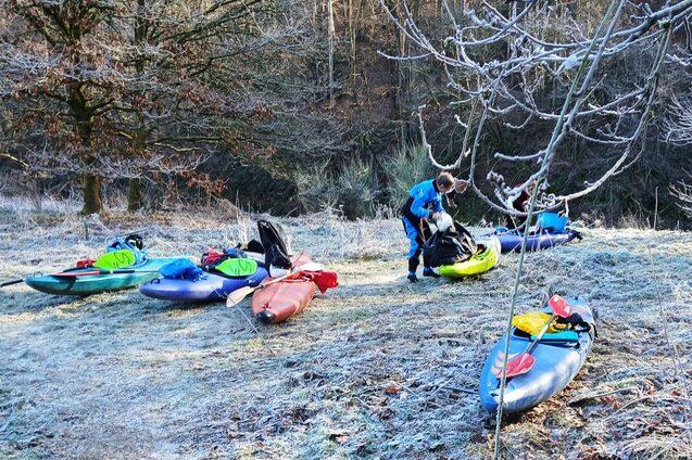 Zwei Personen packen Kajaks auf frostigem Ufer, umgeben von B&auml;umen und einer unber&uuml;hrten Winterlandschaft.