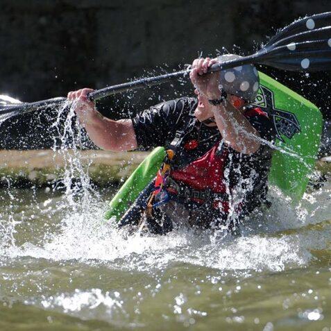 Paddler in einem Kajak, der mit einem Doppelblatts paddelt, spritzt Wasser in einem ruhigen Gew&auml;sser.