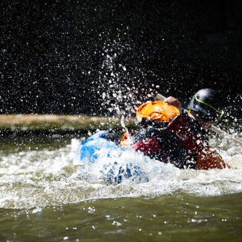 Kajakfahrer in hellem Outfit paddelt durch spritziges Wasser in einem Fluss.