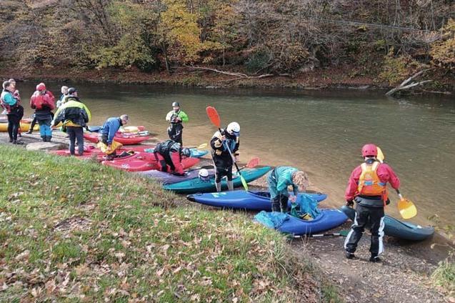 Gruppe von Kajakfahrern bereitet sich am Ufer eines Flusses mit bunten Booten und Ausr&uuml;stung auf einen Ausflug vor.