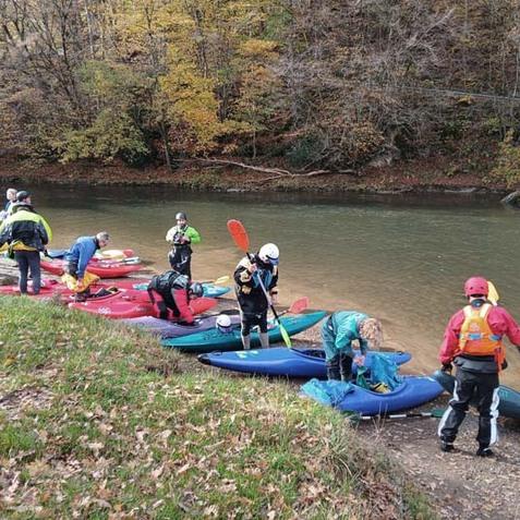 Gruppe von Kajakfahrern bereitet sich am Ufer eines Flusses mit bunten Booten und Ausr&uuml;stung auf einen Ausflug vor.
