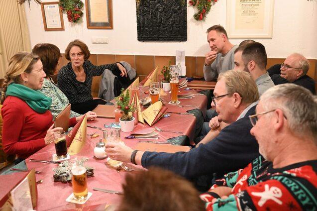 Eine Gruppe von Menschen sitzt an einem Tisch, unterh&auml;lt sich und trinkt Bier in einem festlich dekorierten Raum.
