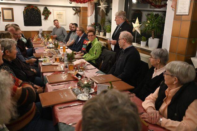 Gesellige Atmosph&auml;re bei einem Abendessen mit mehreren G&auml;sten an einem langen Tisch in einem festlich dekorierten Raum.