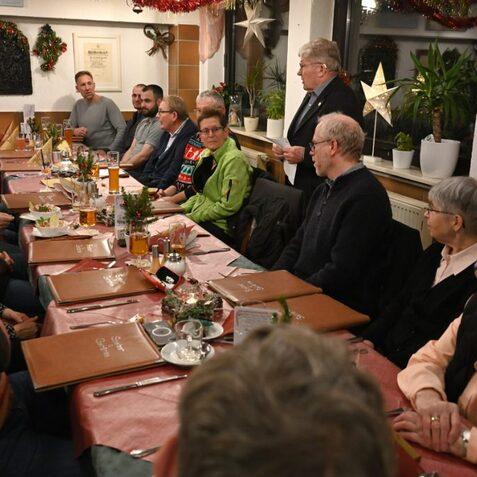 Gesellige Atmosph&auml;re bei einem Abendessen mit mehreren G&auml;sten an einem langen Tisch in einem festlich dekorierten Raum.