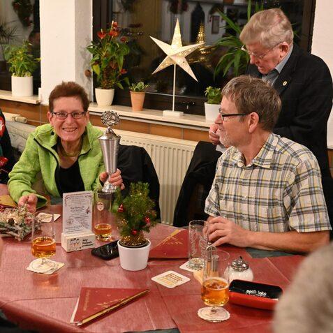 Frau mit einem Pokal in der Hand sitzt an einem Tisch, umgeben von Getr&auml;nken und festlicher Dekoration.