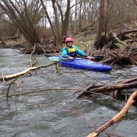 Kajakfahrer auf einem schmalen Fluss, umgeben von &Auml;sten und B&auml;umen im Hintergrund.
