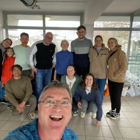 Selbstportr&auml;t einer Gruppe von zehn Personen in einem hellen Raum, mit Fensterblick auf die Stadt im Hintergrund.
