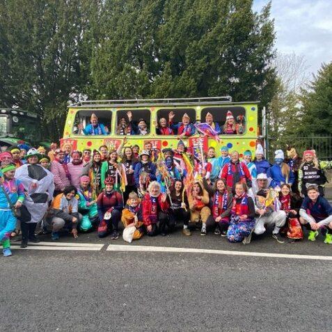 Gruppe von fr&ouml;hlichen Menschen in bunten Kost&uuml;men vor einem festlich geschm&uuml;ckten Bus, der in der Natur steht.