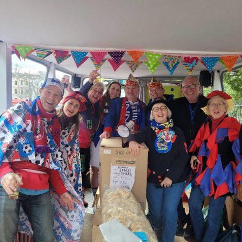 Gruppe von fr&ouml;hlichen Menschen in Kost&uuml;men und H&uuml;ten, die in einem bunten Fahrzeug feiern und feiern.