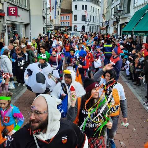 Bunte Menschenmenge in Kost&uuml;men feiert auf einer Stra&szlig;e, umgeben von Geb&auml;uden und Zuschauern. Klarer Karnevalsstimmung.
