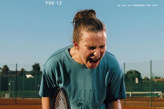 Junge Frau mit Tennisschl&auml;ger auf einem Tennisplatz, ausdrucksstark und energisch, im Hintergrund ein Tennisnetz.