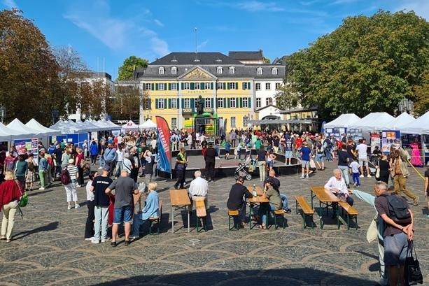 Belebter Marktplatz mit Verkaufsst&auml;nden, Besuchern und historischer Architektur im Hintergrund.