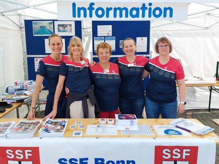 F&uuml;nf Frauen in einheitlichen T-Shirts stehen am Informationsstand des SSF Bonn unter einem Zelt.