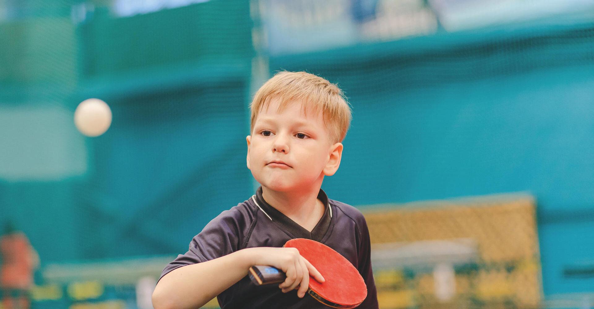 Junge mit Tischtennisschl&auml;ger in der Hand schaut konzentriert auf einen Ball, der ihm entgegenfliegt.