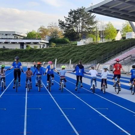 Gruppe von Kindern und Erwachsenen auf Einr&auml;dern, die auf blauer Rennbahn stehen und H&auml;nde halten.