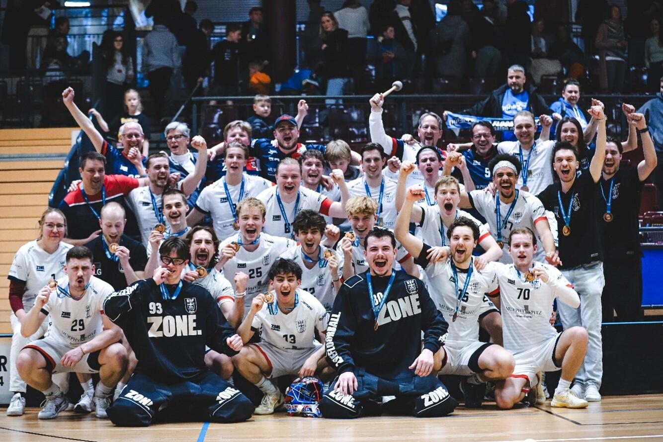 Feiernde Mannschaft mit Medaillen in Sportkleidung posiert l&auml;chelnd auf dem Spielfeld nach einem Sieg.