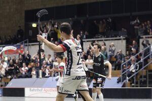Ein Spieler jubelt nach einem Tor in der Halle, Zuschauer feiern im Hintergrund. Sportevent mit Emotionen.