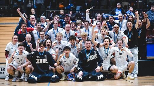 Feiernde Mannschaft mit Medaillen in Sportkleidung posiert l&auml;chelnd auf dem Spielfeld nach einem Sieg.