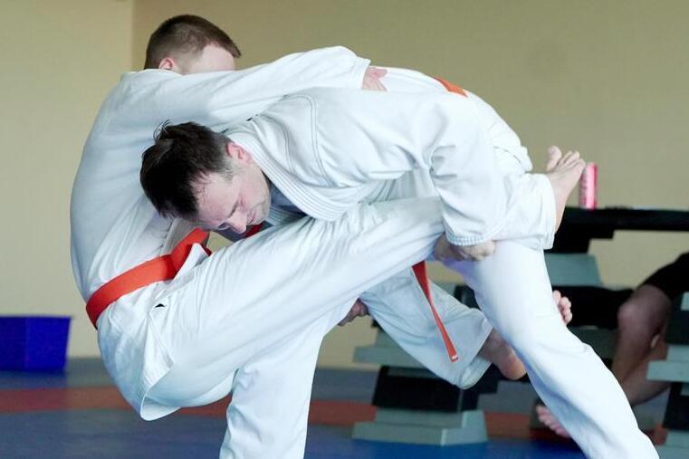 Zwei Judokas im wei&szlig;en Gi k&auml;mpfen auf einer blauen Matte; einer f&uuml;hrt eine Wurftechnik aus.
