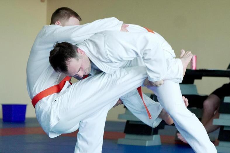 Zwei Judokas im wei&szlig;en Gi k&auml;mpfen auf einer blauen Matte; einer f&uuml;hrt eine Wurftechnik aus.