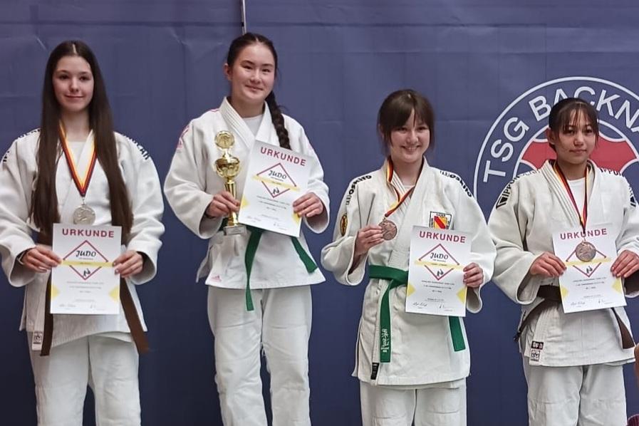 Vier Judokas stehen auf dem Siegertreppchen, jede mit Medaille und Urkunde in der Hand.