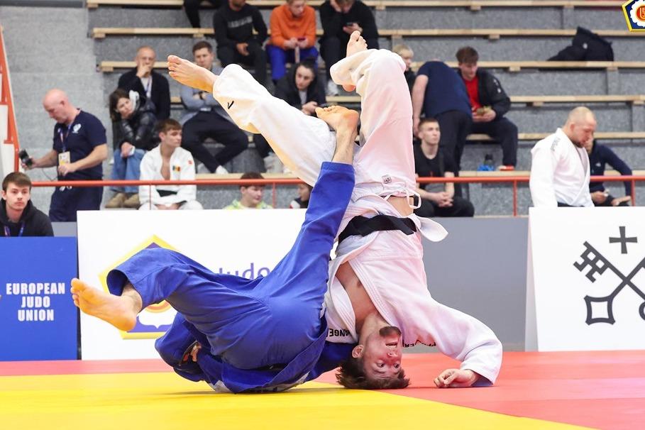 Zwei Judokas in wei&szlig;en und blauen Anz&uuml;gen k&auml;mpfen auf einer tatami, w&auml;hrend Zuschauer im Hintergrund zuschauen.