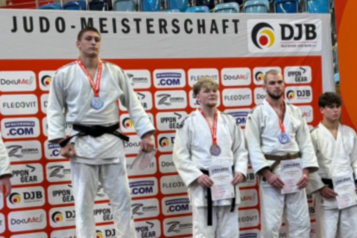 Zwei Gruppen junger Judokas mit Medaillen auf der Deutschen Judo-Meisterschaft vor einem Banner mit Sponsorenlogos.