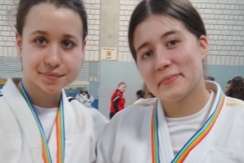 Zwei junge Judokas mit Medaillen in wei&szlig;en Anz&uuml;gen stehen l&auml;chelnd in einer Sporthalle.