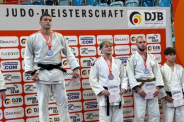 Zwei Gruppen junger Judokas mit Medaillen auf der Deutschen Judo-Meisterschaft vor einem Banner mit Sponsorenlogos.