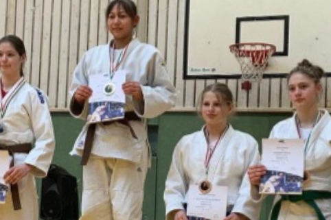 Mehrere Jugendliche in Karateanz&uuml;gen stehen auf einem Podest mit Medaillen und Urkunden in der Hand.