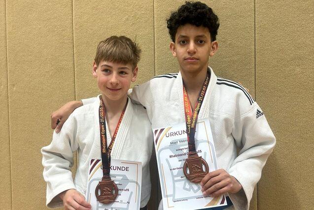 Zwei Judoka in wei&szlig;en Anz&uuml;gen halten stolz ihre Urkunden und Medaillen f&uuml;r den dritten Platz in der Hand.