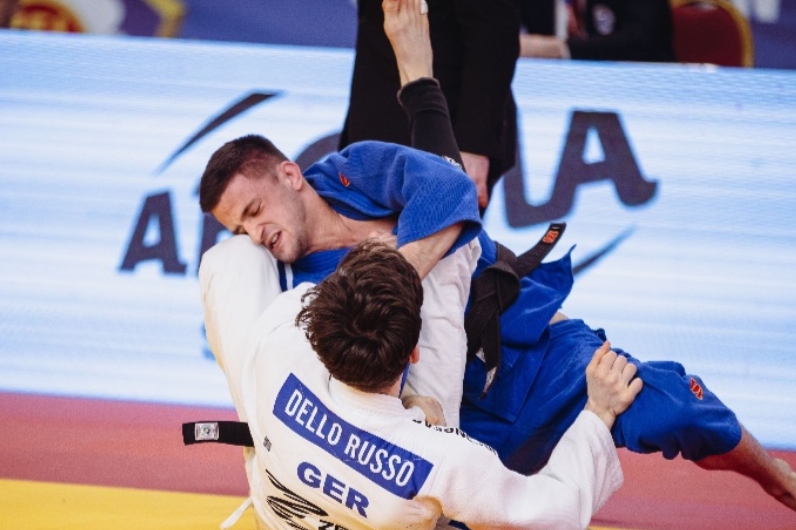 Zwei Judo-K&auml;mpferinnen in blauen und wei&szlig;en Anz&uuml;gen k&auml;mpfen oben, w&auml;hrend zwei m&auml;nnliche Judoka unten gegeneinander antreten.