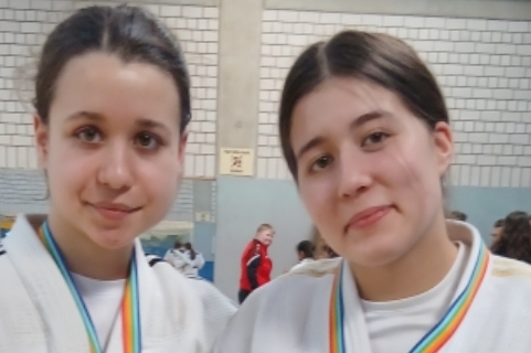 Zwei junge Judokas mit Medaillen in wei&szlig;en Anz&uuml;gen stehen l&auml;chelnd in einer Sporthalle.