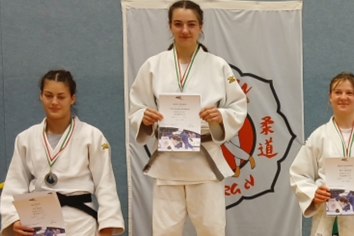 Gruppenfoto von Judokas in Mats, die Medaillen und Urkunden halten, vor einer Wand mit Judokas-Logo.
