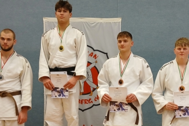 Gruppenfoto von Judokas in Mats, die Medaillen und Urkunden halten, vor einer Wand mit Judokas-Logo.