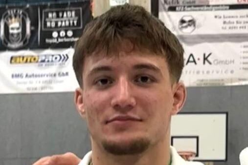 Junger Mann in Judokleidung mit Medaille um den Hals, steht vor einem Hintergrund mit sportlichen Plakaten.