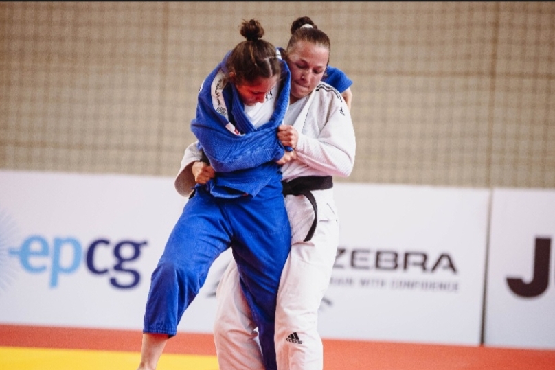 Zwei Judo-K&auml;mpferinnen in blauen und wei&szlig;en Anz&uuml;gen k&auml;mpfen oben, w&auml;hrend zwei m&auml;nnliche Judoka unten gegeneinander antreten.