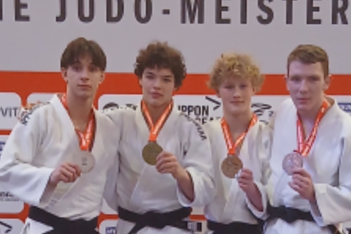 Zwei Gruppen junger Judokas mit Medaillen auf der Deutschen Judo-Meisterschaft vor einem Banner mit Sponsorenlogos.