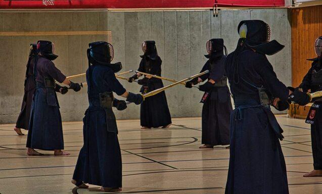 Gruppentraining von Kendo-Praktizierenden in &Uuml;bungshaltung mit Bambusschwertern in einer Turnhalle.
