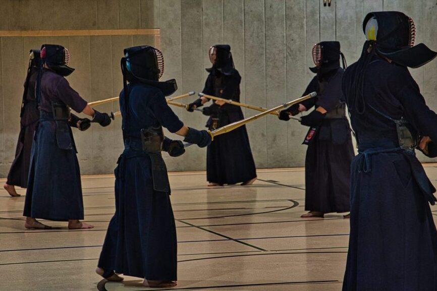 Gruppentraining von Kendo-Praktizierenden in &Uuml;bungshaltung mit Bambusschwertern in einer Turnhalle.