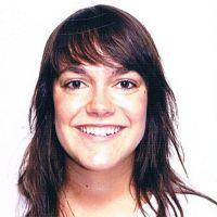 Portr&auml;t einer l&auml;chelnden Frau mit langen, braunen Haaren vor einem einfarbigen Hintergrund.