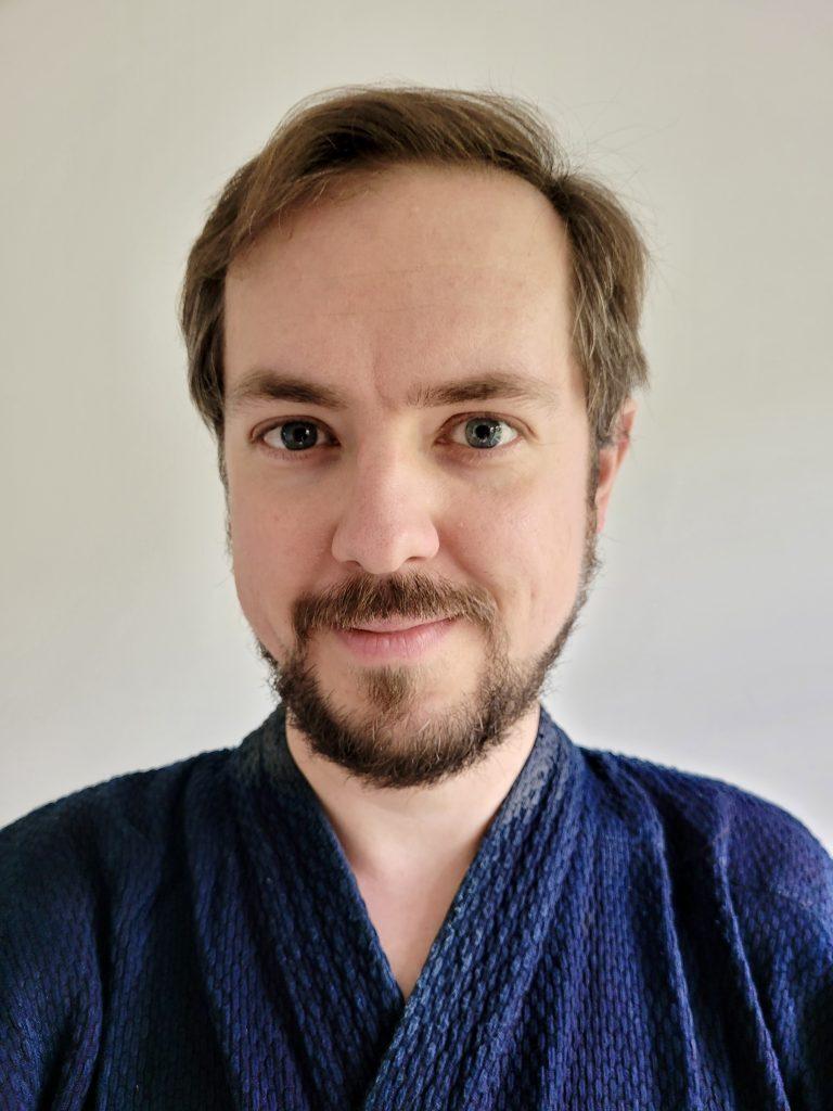 Portr&auml;t eines Mannes mit Bart und blauen Kimono, vor neutralem, hellem Hintergrund.