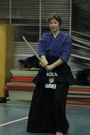 K&auml;mpferin in blauem Kimono h&auml;lt ein Holzschwert in angreifender Position in einer Sporthalle.