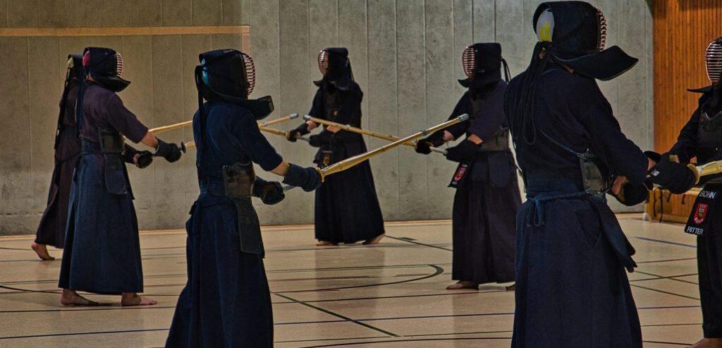 Gruppentraining von Kendo-Praktizierenden in &Uuml;bungshaltung mit Bambusschwertern in einer Turnhalle.