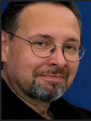 Mann mit Brille und Bart vor einem Poster mit einem Bogensch&uuml;tzen in traditioneller Kleidung.