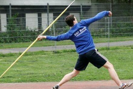 Ein Sportler wirft einen Speer auf einer Laufbahn, w&auml;hrend er sich in einer dynamischen Wurfbewegung befindet.