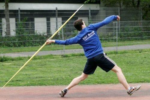 Ein Sportler wirft einen Speer auf einer Laufbahn, w&auml;hrend er sich in einer dynamischen Wurfbewegung befindet.